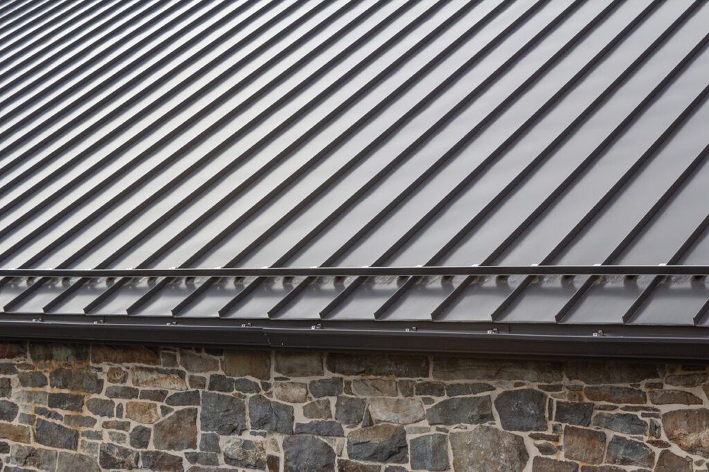 Standing seam modern metal roof over vintage stone wall, horizon