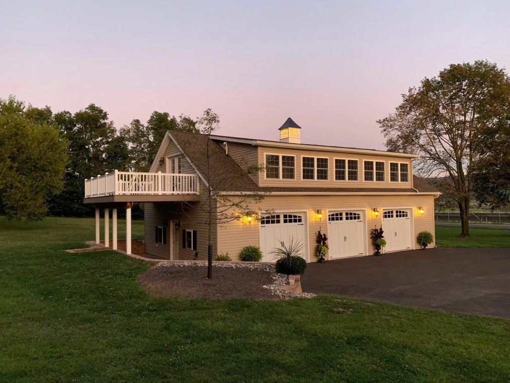 A custom-built, two-door garage with cream siding, white trim, lights, and a veranda above a side door to the left
